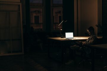 man in een donkere kamer zit naast een tafel met daarop een laptop, als afbeelding bij een blog over mijnpensioenoverzicht