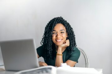 vrouw achter haar laptop, lachend naar de camera als afbeelding bij artikel over het vinden van een goede pensioenadviseur