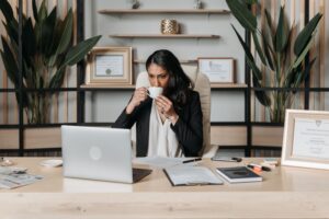 Vrouw achter een bureau naar laptop kijkend drinkt koffie als illustratie bij blog over zorgtoeslag