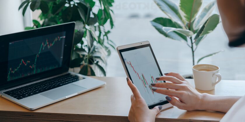 Vrouw zit met een tablet achter haar computer en kijkt naar een grafiek als afbeelding bij een blog over hoeveel pensioen kun je aankopen