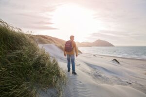 Man staat in de duinen naar het strand en de zee met een rugzak op, als afbeelding bij een blog over werkgever pensioencoach