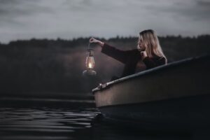 Vrouw alleen in een roeiboot in de schemer met een lamp in haar hand als afbeelding bij een blog over de pensioendip