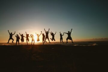 een groep mensen danst op het strand bij ondergaande zon als afbeelding bij een blog over levenskwaliteit