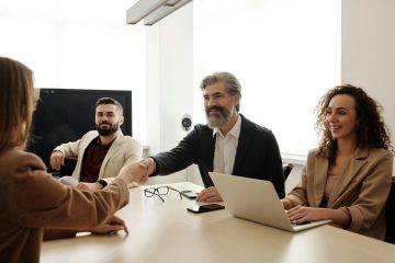 Man geeft een handdruk tijdens een setting aan een bureau met meerdere mensen als illustratie bij RVU-regeling en transitievergoeding