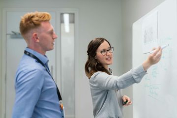 vrouw legt uit aan een man op een whiteboard als illustratie bij een blog met uitleg over AOW en minimumloon